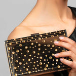 Model holding the Parker black lucite clutch which is embellished with various size gold Austrian crystals in a polka dot design