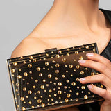 Model holding the Parker black lucite clutch which is embellished with various size gold Austrian crystals in a polka dot design