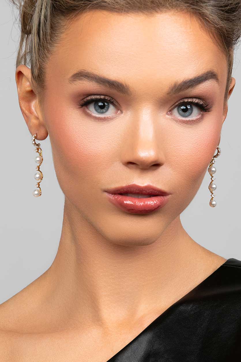 Model wearing the Ariel Taub Pearla earrings in gold which are a long drop containing 3 pearls and pave CZ crystals in between the pearls