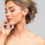 Model turning headwearing the Ariel Taub Pearla earrings in gold which are a long drop containing 3 pearls and pave CZ crystals in between the pearls