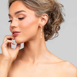 Model turning headwearing the Ariel Taub Pearla earrings in gold which are a long drop containing 3 pearls and pave CZ crystals in between the pearls