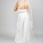 A bride wearing a white chapel veil with floral lace design and Austrian pearl embellishments, posing with her back to the camera.