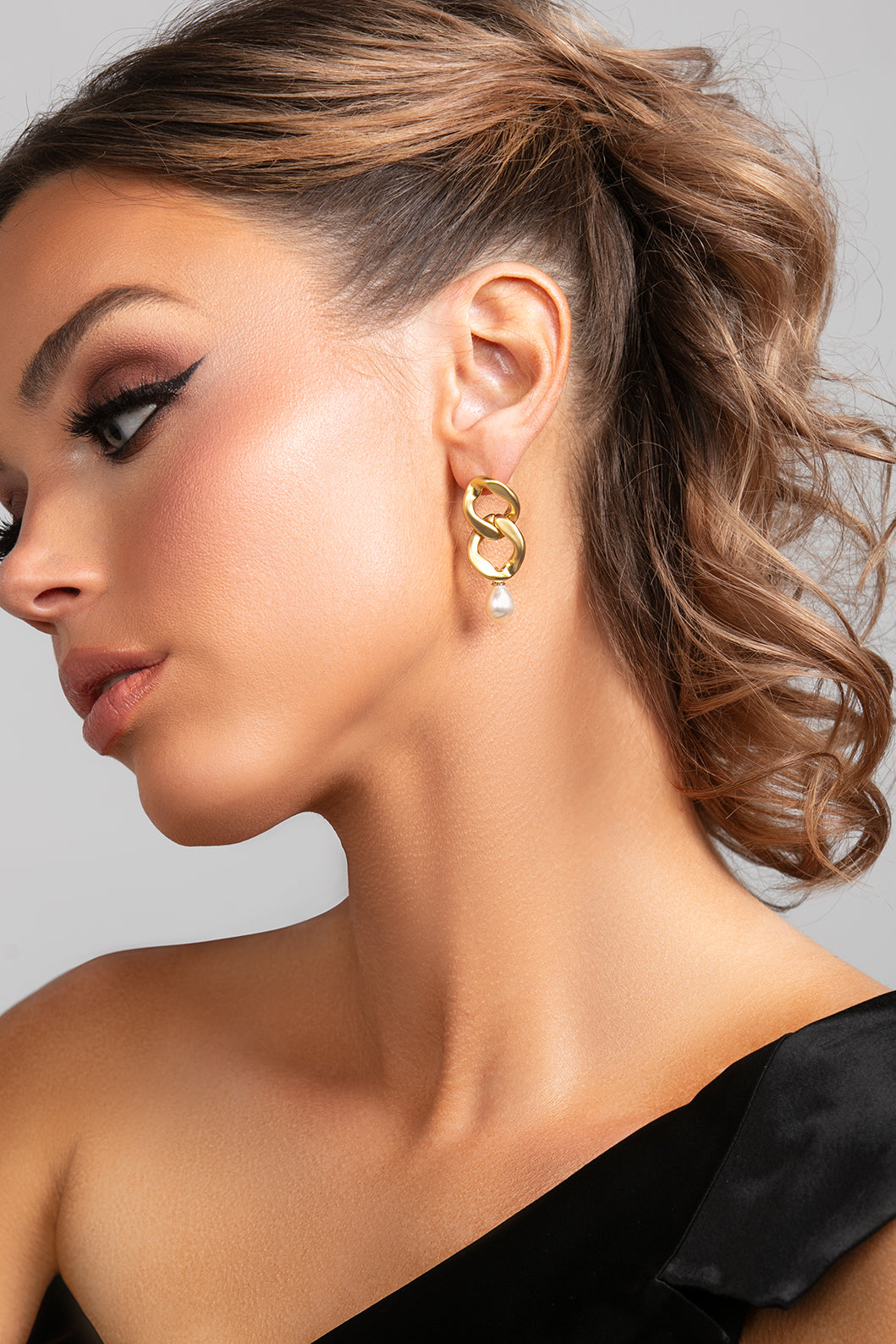 Model wearing the Serena earrings in gold which is a chain link earring with a pearl drop