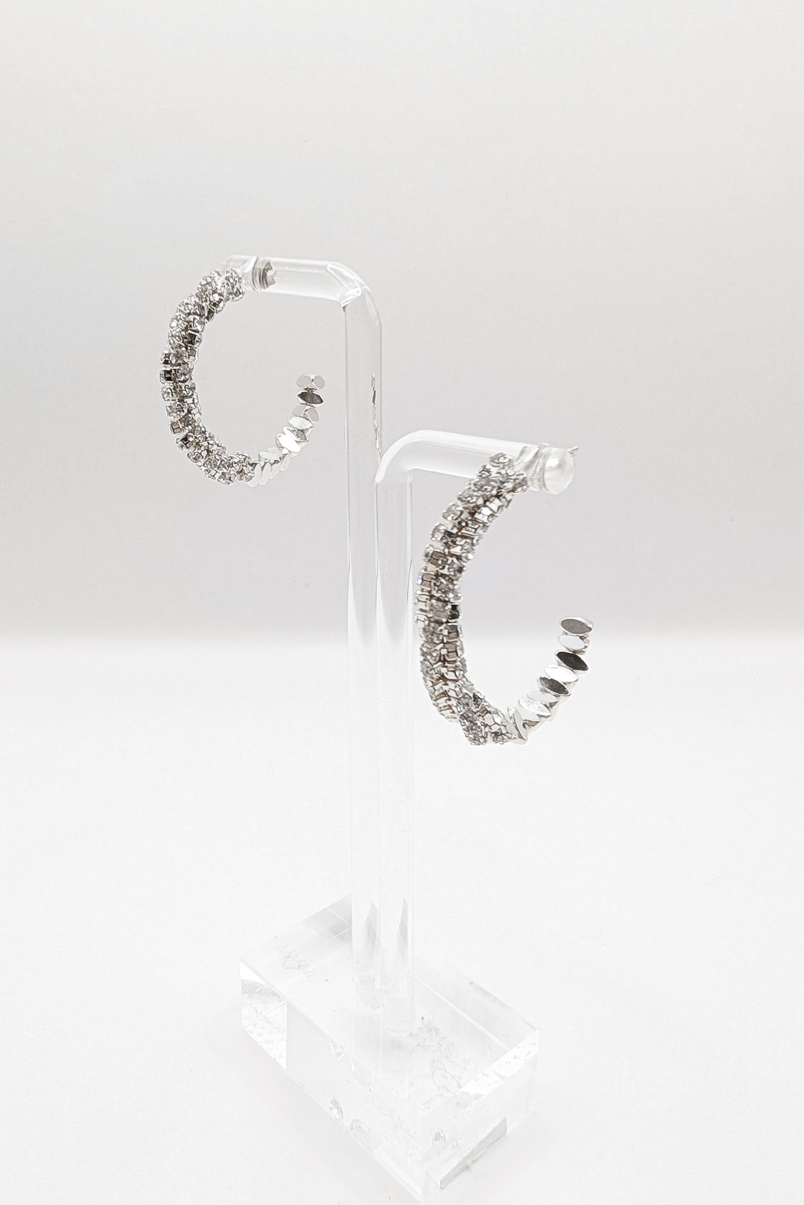 Sparkle CZ pave crystal hoop earrings show in silver on an earring stand.