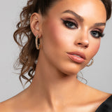 Model wearing a statement pave crystal large hoop earrings in gold