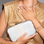 Woman in a gold dress holding an off white pearl clutch against a gray background