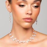 Woman wearing a pearl necklace and earrings against a gray background