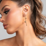 Close-up of model wearing the Sawyer earrings in gold, showing the lightweight linear drop design with polished metal spheres.