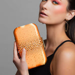 Woman holding an orange Austrian crystal clutch with teal lining in honor of Taylor Swift's Life of a Showgirl album against a gray background