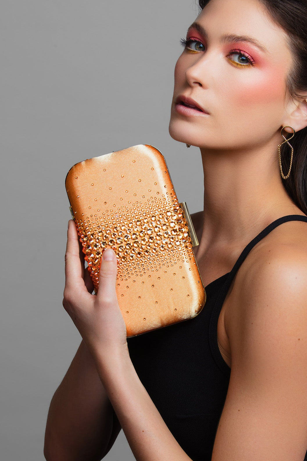 Model holding Ariel Taub’s orange crystal clutch with teal satin lining, Taylor Swift inspired accessory paired with the Lexie gold infinity earrings.