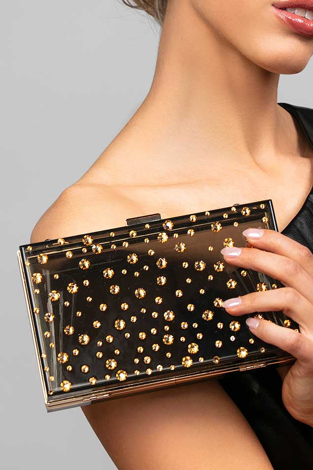 Model holding the Parker black lucite clutch which is embellished with various size gold Austrian crystals in a polka dot design