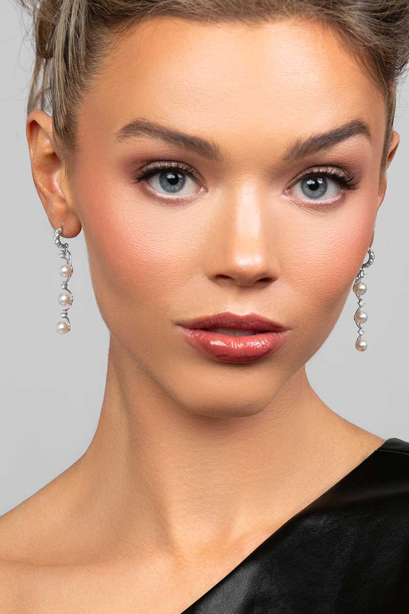 Model wearing the Ariel Taub Pearla earrings in silver which are a long drop containing 3 pearls and pave CZ crystals in between the pearls