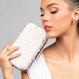 Model holding a blush satin clutch embellished with pearls and crystals in a polka dot design