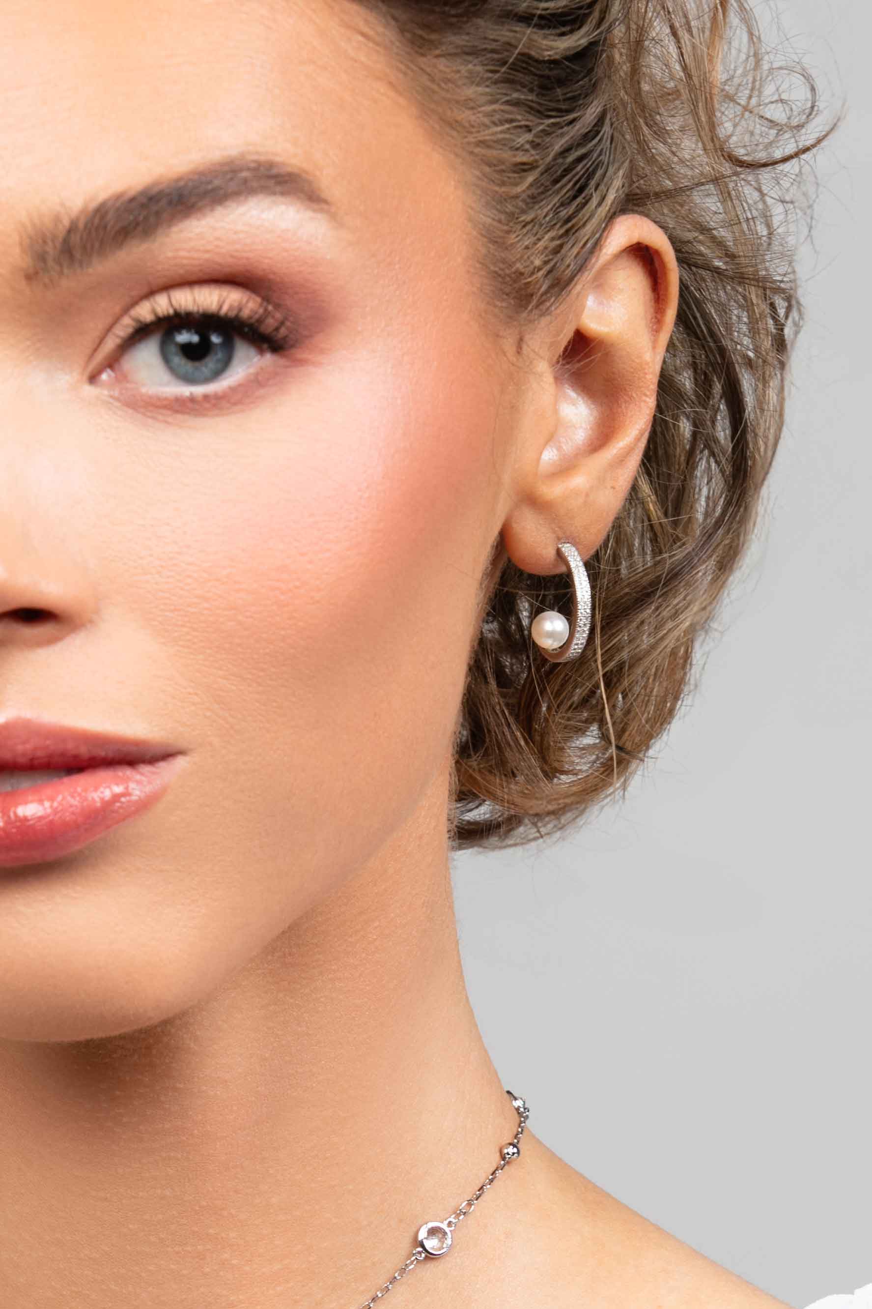 Model wearing the Prim cubic zirconia pave crystal partial hoop earrings with a floating pearl on the inside