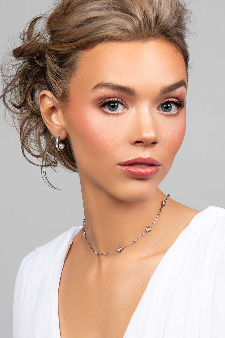 Model wearing the Prim cubic zirconia pave crystal partial hoop earrings with a floating pearl on the inside paired with a crystal choker