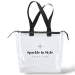 Sparkle in Style clear tote bag by Ariel Taub – Medium-sized transparent tote with black handles and zipper, featuring the phrase 'Sparkle in Style' on the front. Stylish and functional design, perfect for everyday use, travel, or shopping. A modern accessory that combines practicality with chic branding.