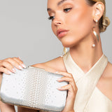 Woman holding a ivory pearl clutch wearing the Taylor gold pearl twist earrings with a sleek bun and gold jumpsuit, against a neutral background