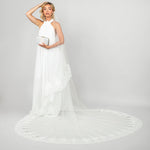 Model wearing the Tiana two-tier cathedral veil with wide corded lace trim by Ariel Taub paired with the Tresor pearl clutch