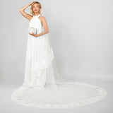 Model wearing the Tiana two-tier cathedral veil with wide corded lace trim by Ariel Taub paired with the Tresor pearl clutch