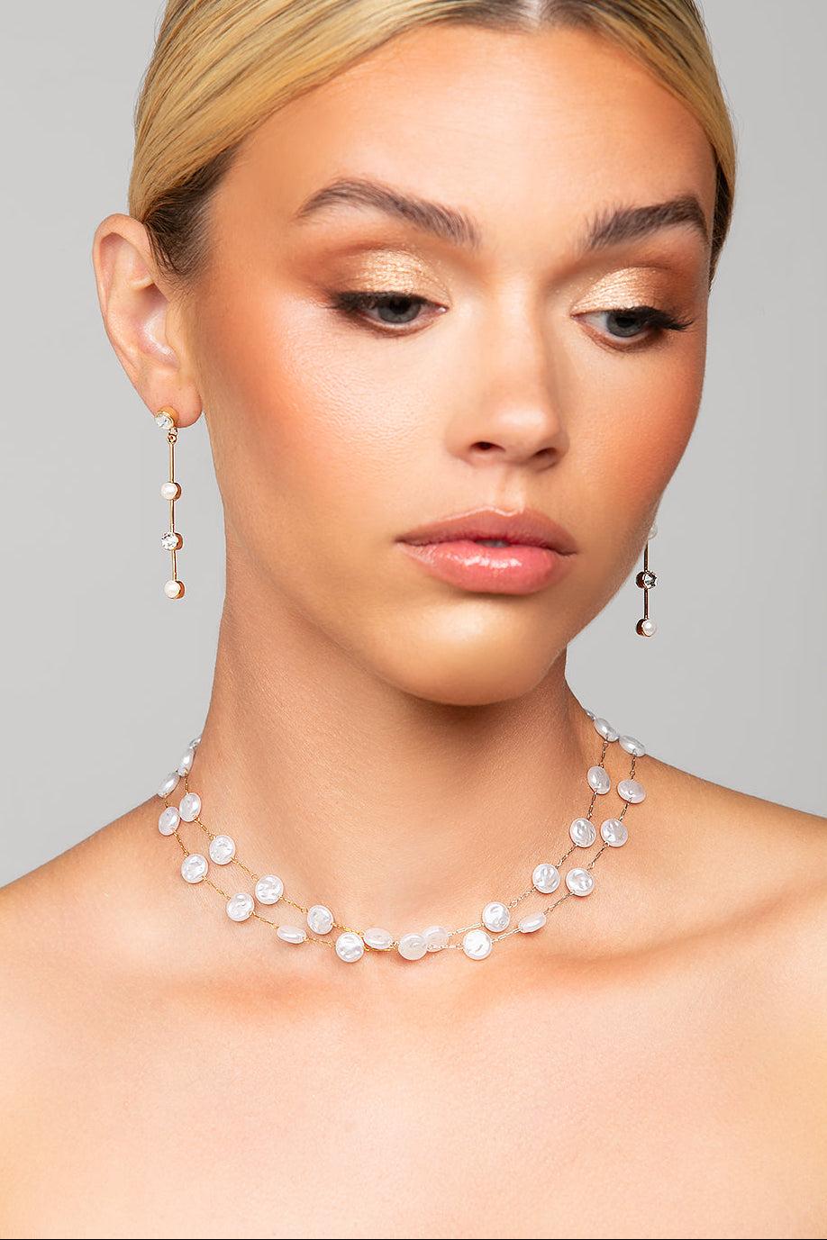 Woman wearing a pearl necklace and earrings against a gray background
