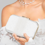 Woman holding a white pearl clutch with a white lacey dress on a plain background