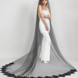 Woman in a white strapless pantsuit dress with a long black veil on a gray background