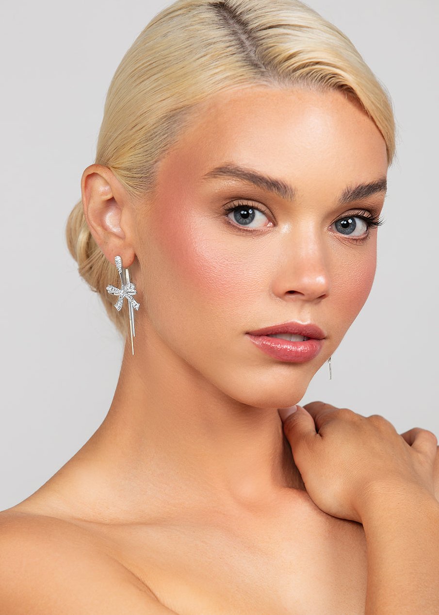 Pave crystal elongated post earrings with a crystal pave rope and pearl bow drop, designed for festive occasions. Shown in rhodium plated silver.