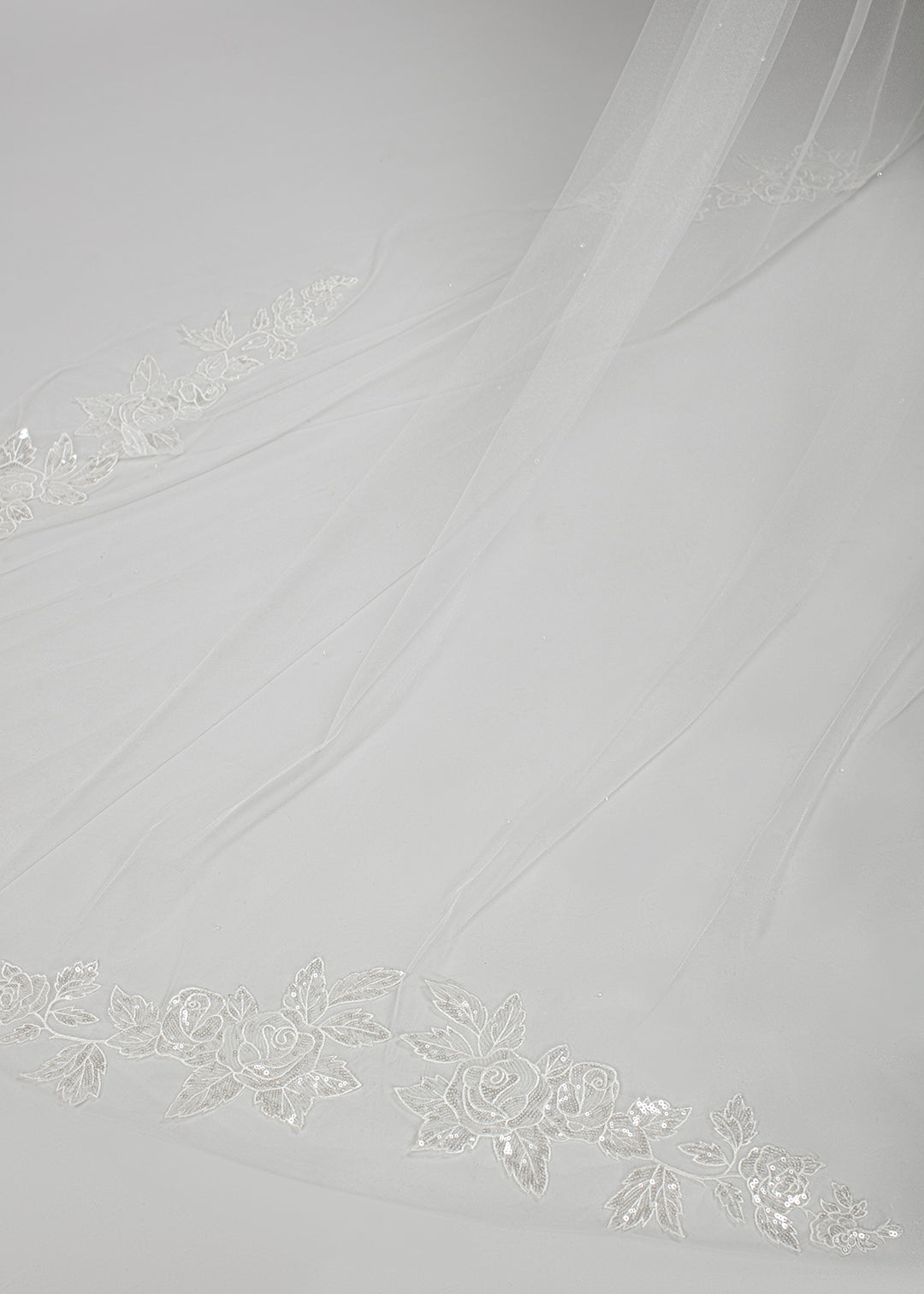 Detail shot of the train of the single-tier cathedral-length veil with sequin rose appliques along the train, inspired by the rose gardens of Versailles, available in ivory and white tones.