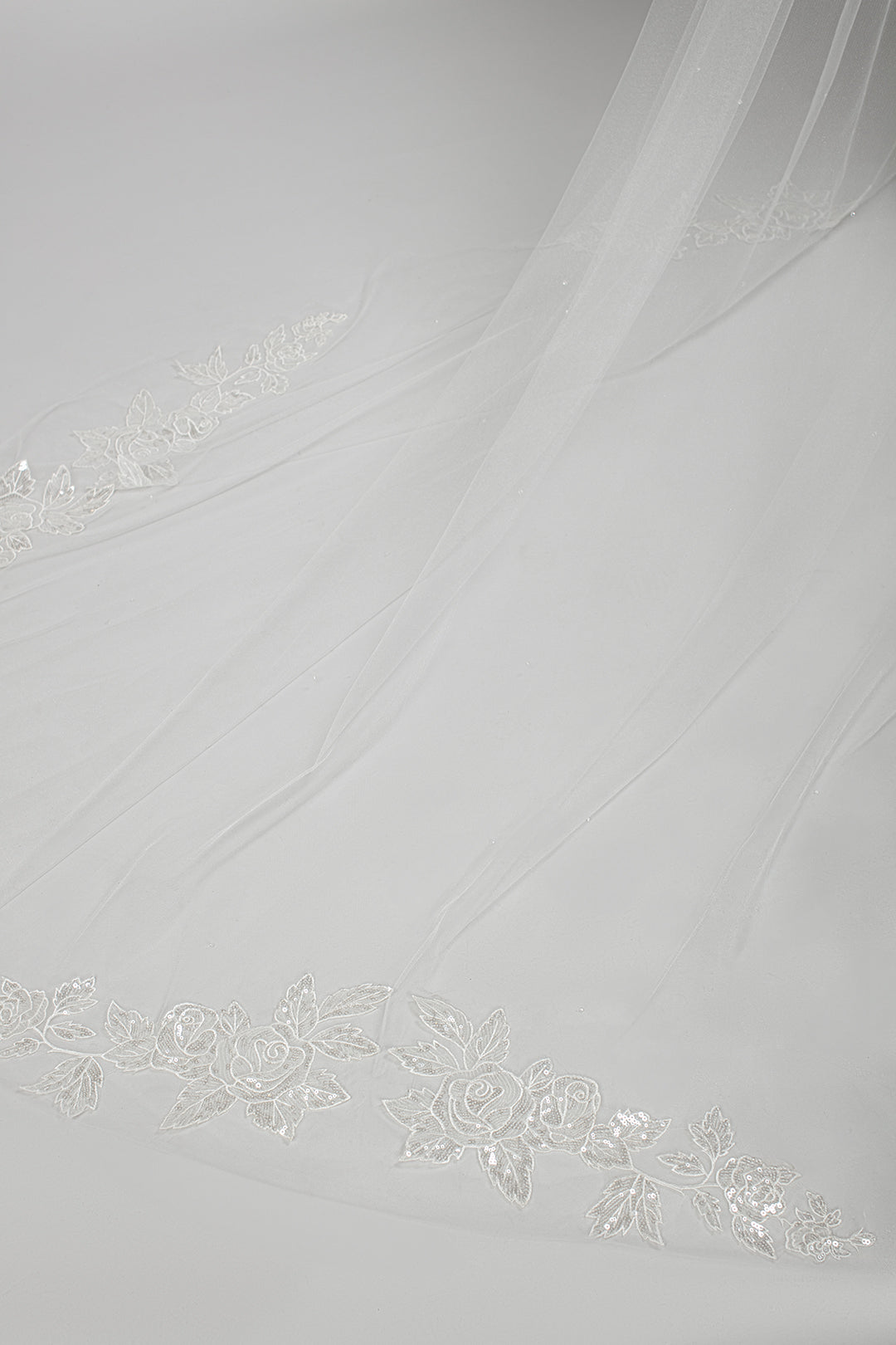 Detail shot of the train of the single-tier cathedral-length veil with sequin rose appliques along the train, inspired by the rose gardens of Versailles, available in ivory and white tones.