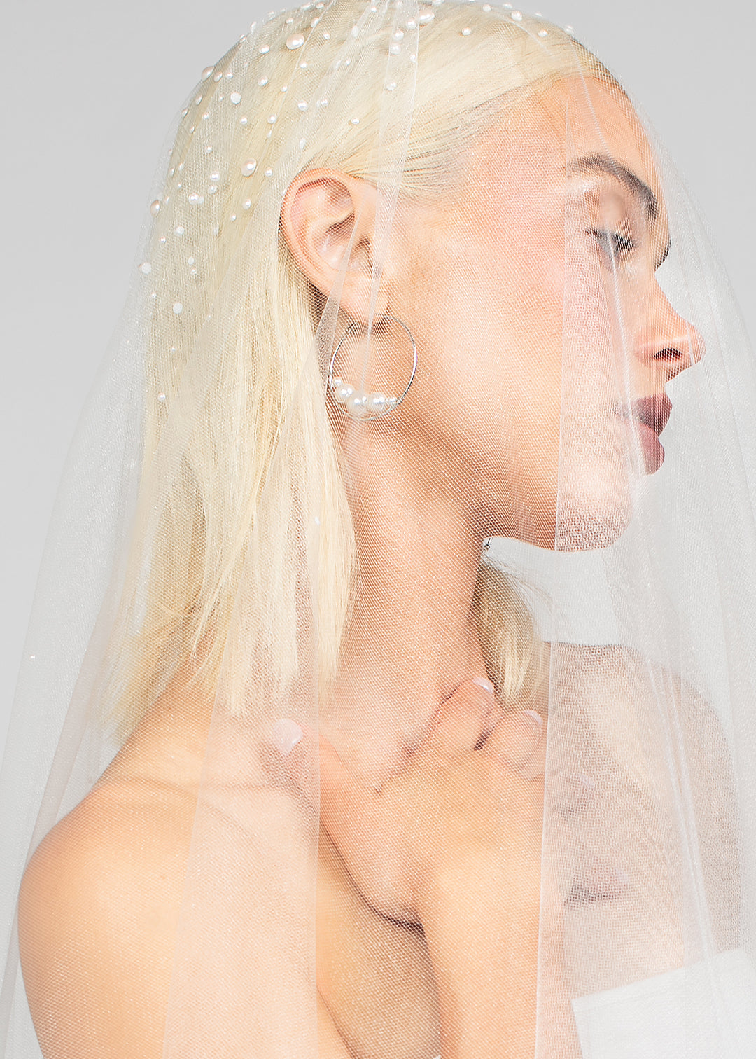 Detail shot of the double tier cathedral-length bridal veil with heavy Austrian pearls clustered at the top paired with the large rhodium plated silver Austrian pearl Rio hoop earrings for a modern day wedding look.