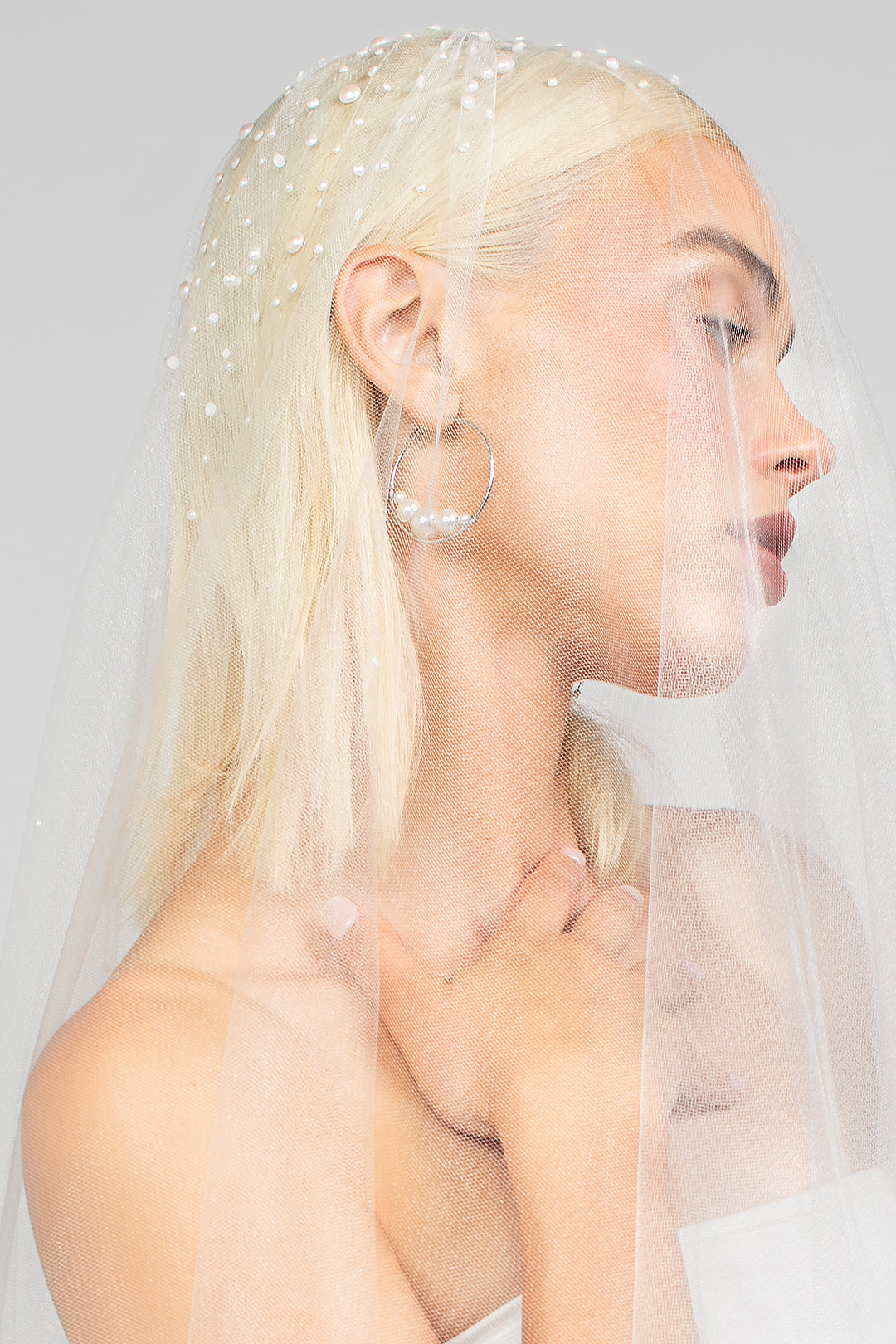 Detail shot of the double tier cathedral-length bridal veil with heavy Austrian pearls clustered at the top paired with the large rhodium plated silver Austrian pearl Rio hoop earrings for a modern day wedding look.