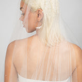 Detail shot of the top of the Royalty bridal veil. Two-tier cathedral-length wedding veil with heavy Austrian pearls clustered at the top, fading into a light scatter toward the bottom, available in multiple shades of white and blush. Paired with the large Austrian hoop Rio earrings in silver.