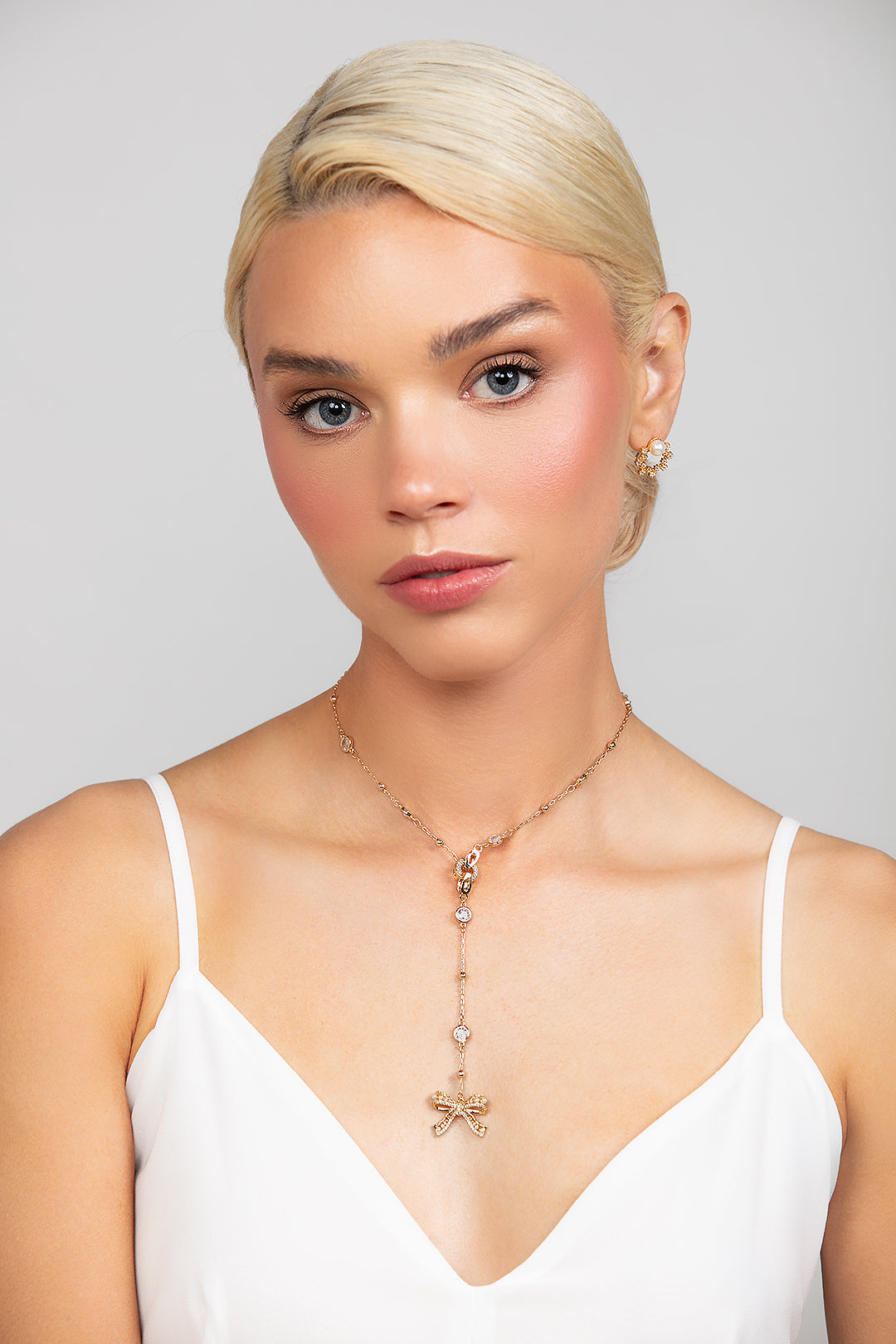 A detachable bow lariat charm necklace attached to a sparkly gold chain that can be worn as a choker as well. Front view shown in gold.