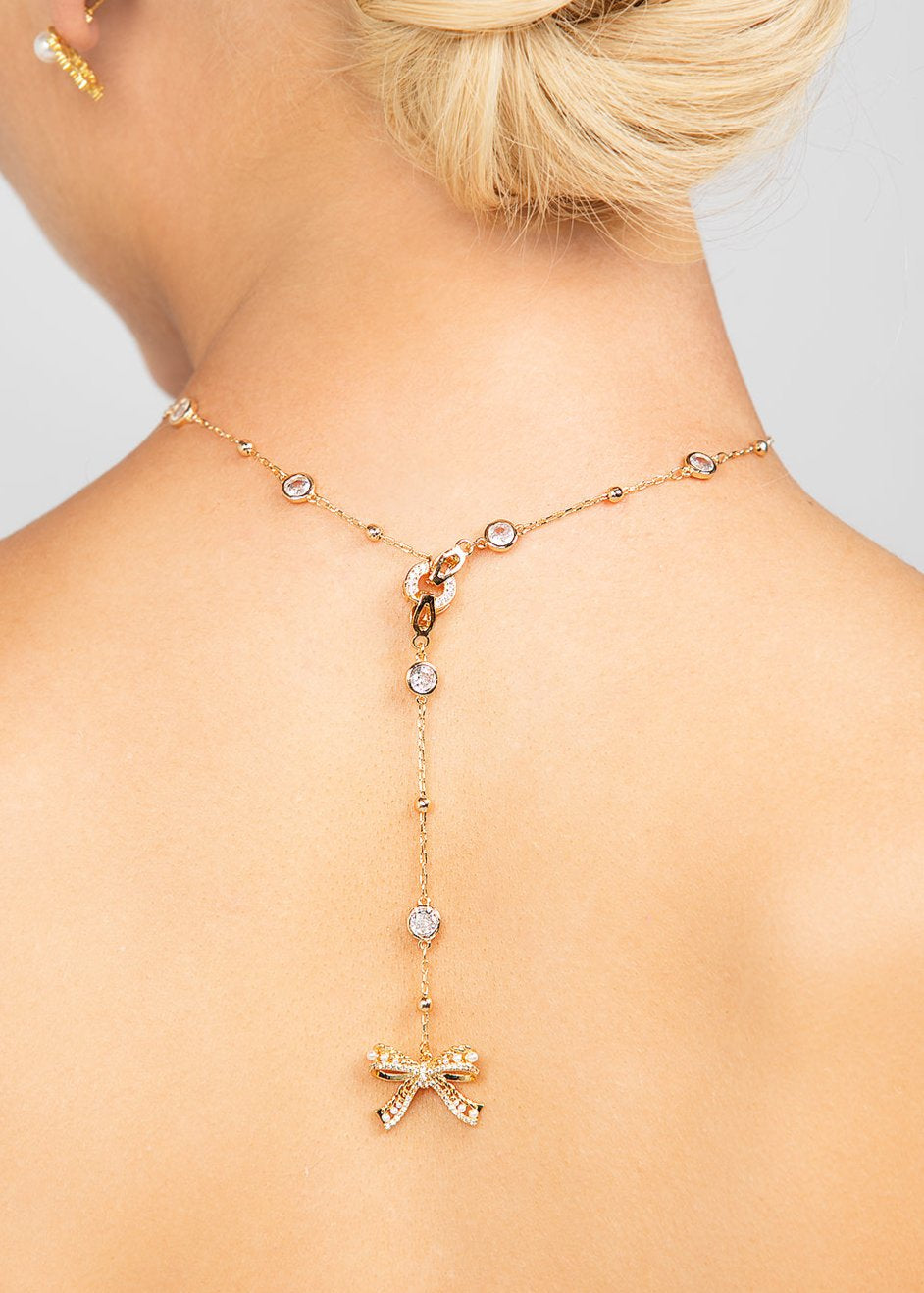 Gold Ryan necklace styled backwards, showcasing its detachable pave crystal bow pendant elegantly draped along the back for a unique and modern bridal or fashion statement.