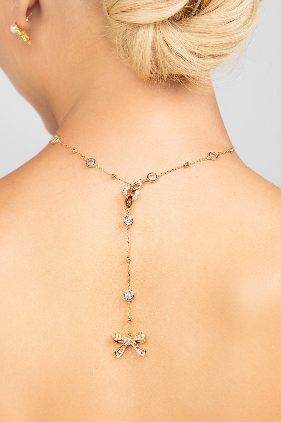 Gold Ryan necklace styled backwards, showcasing its detachable pave crystal bow pendant elegantly draped along the back for a unique and modern bridal or fashion statement.