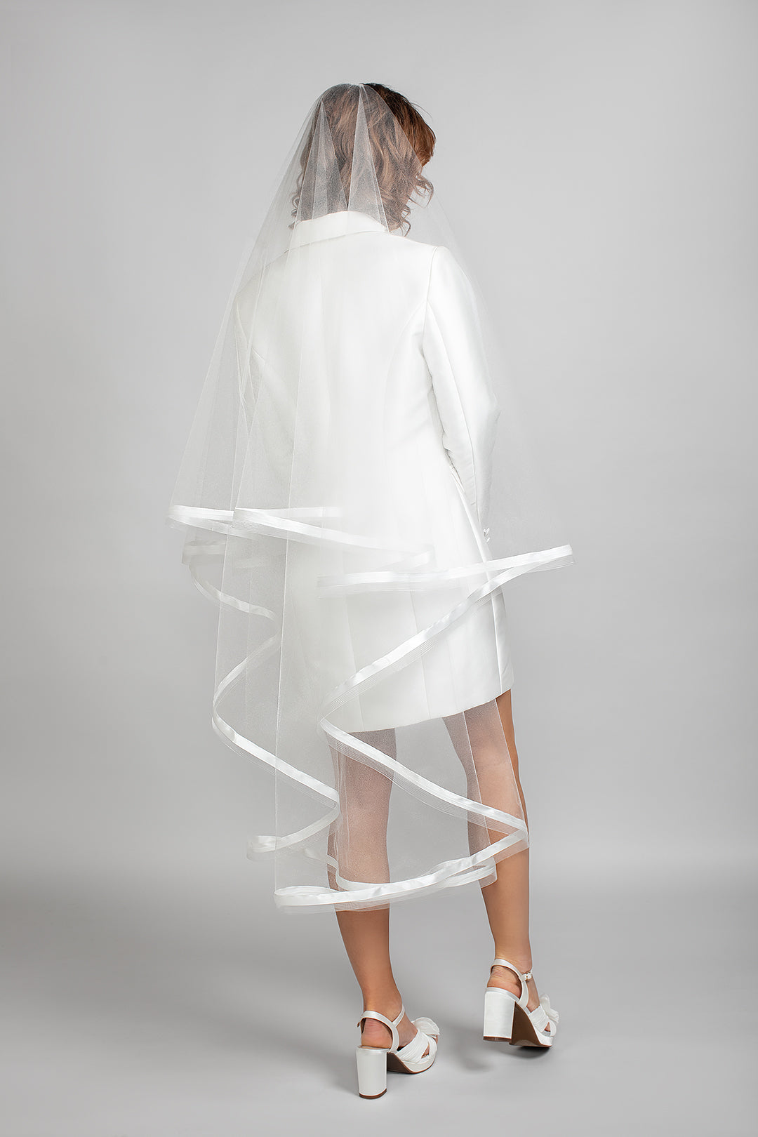 Back view of the Sadie veil featuring two tiers with 1" satin and horsehair trim, draping over a white Andrea Osei BRIDE tailored Renee blazer dress.