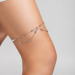 Close-up of a model wearing the Shimmer garter on her thigh, featuring delicate silver chains with crystal accents and a custom crystal initial charm, styled with a white mini dress.