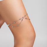 Close-up of a model wearing the Shimmer garter on her thigh, featuring delicate silver chains with crystal accents and a custom crystal initial charm, styled with a white mini dress.