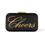Front view of the Stella clutch featuring the word “Cheers” written in gold Austrian crystals on a black satin box bag with a gold clasp.