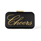 Front view of the Stella clutch featuring the word “Cheers” written in gold Austrian crystals on a black satin box bag with a gold clasp.